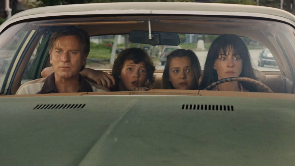 The Platt family — Greg (Ewan McGregor), Brian (Christian Convery), Audrey (Maisy Stella) and Denise (Anne Hathaway) — sit tense and wide-eyed inside a vintage car, staring out through the windscreen in a scene from "The End of Oak Street" (2026).